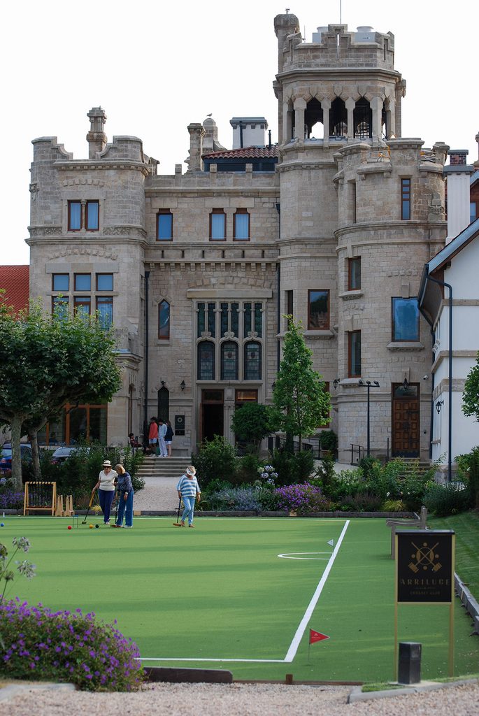 The historic, stone façade of Palacio Arriluce Hotel overlooking a perfectly manicured, vibrant green lawn of an official croquet court in Getxo, Spain