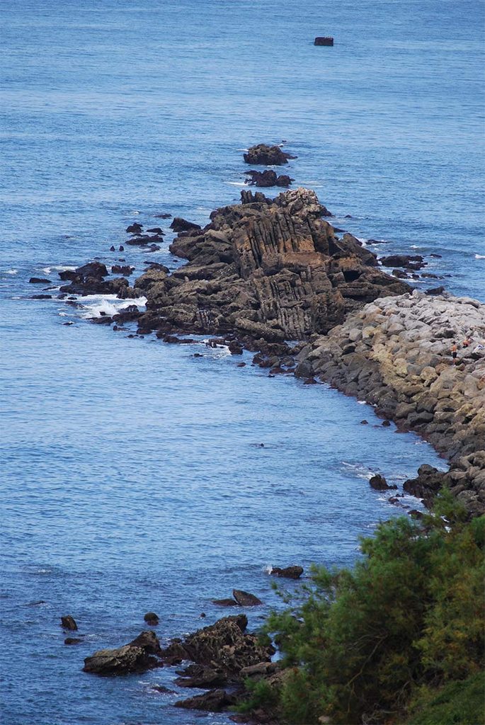 A scenic view of a calm blue sea stretching out next to a rugged, rocky coastline under a clear sky.